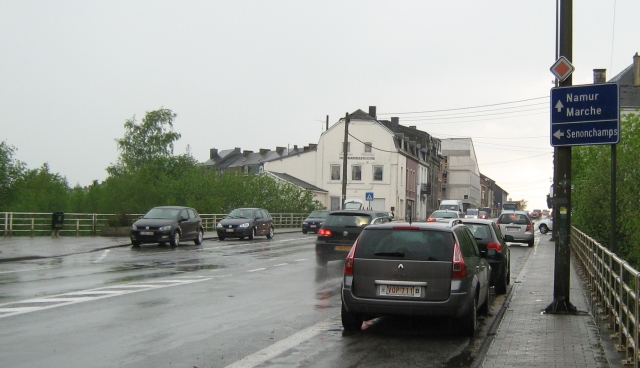 a wet street in bastogne with wet cars and houses